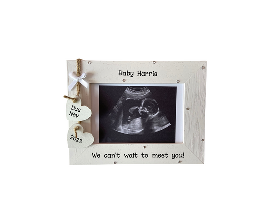 Image shows baby scan wooden photo frame, decorated with two hanging hearts with due date, attached to small bow, gems can be added.