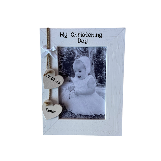 Image shows. wooden christening day frame with two hanging hearts with a name and date, also including a small white bow above.