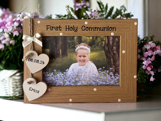 Image shows brown vintage first holy communion photo frame, decorated with cream polka dots and two cream hanging hearts with name and date attached to string and cream bow.