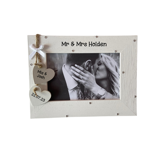 Image shows mr and mrs wedding photo frame, includes two hanging hearts with couples names and wedding date, also a small white bow. Bling can be added.