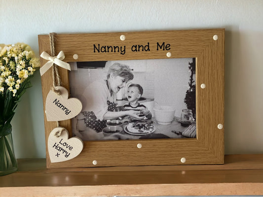 Image shows photo frame for nanny, consists of a brown wooden frame with cream dots, two cream hanging hearts for names and a cream bow to sit above.