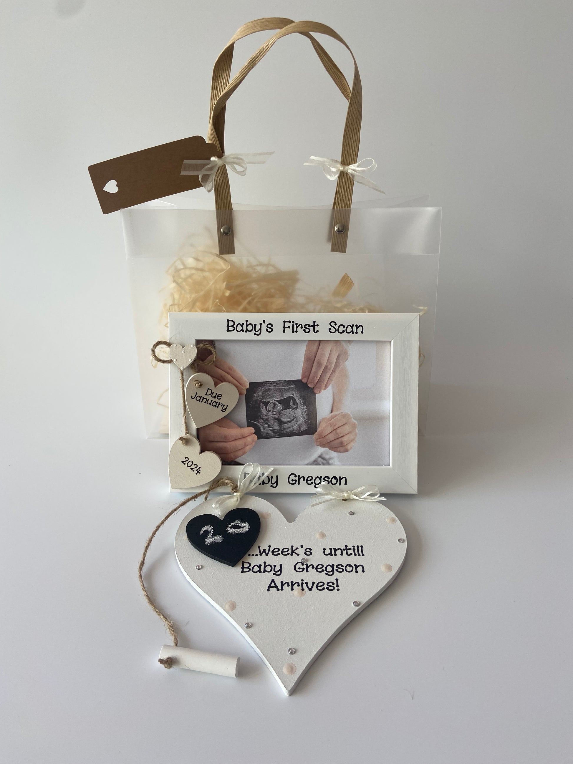 Image shows a baby's first scan matching photo frame and plaque gift set. Photo frame consists of two hanging hearts with due date and a small heart placed above with with polka dots. Plaque decorated with polka dots, gems and ribbon, with a piece of chalk attached in order to count down the weeks to the due date. Also includes gift wrap and photo of your choice.