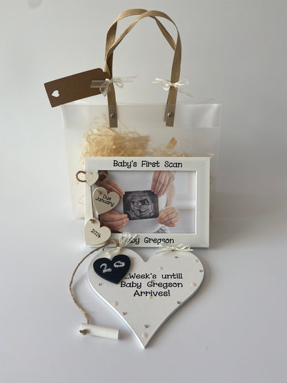 Image shows a baby's first scan matching photo frame and plaque gift set. Photo frame consists of two hanging hearts with due date and a small heart placed above with with polka dots. Plaque decorated with polka dots, gems and ribbon, with a piece of chalk attached in order to count down the weeks to the due date. Also includes gift wrap and photo of your choice.
