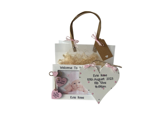 Image shows pairing plaque and photo frame included in this new born gift set, plaque is decorated with polka dots, bling and ribbon, photo frame consists of two hanging hearts to include baby's date of birth, time of birth and weight. Gift wrap and photo included.