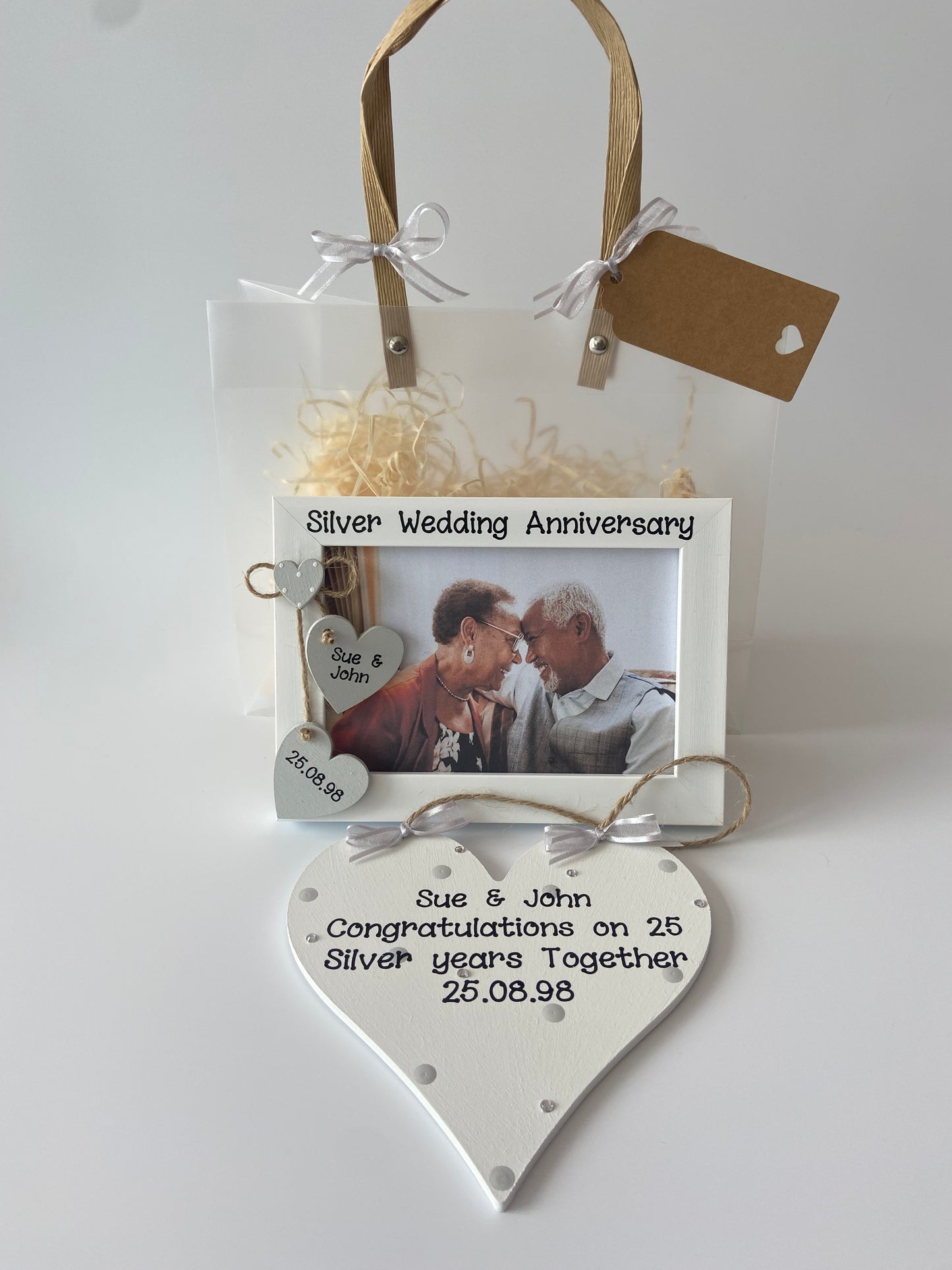 Image shows wedding anniversary gift set including a photo frame and plaque, decorated with polka dots, gems and ribbon. Frame with two hearts with the couples names and wedding date. Includes gift wrap and photo.