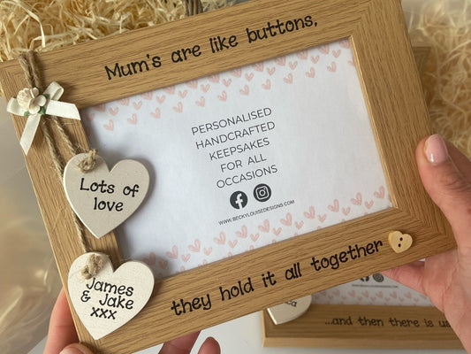 Image shows mum quote vintage photo frame, decorated with two cream hearts with children's names attached to string, a cream bow and small cream flower, at the end of the quote sits a small wooden heart.