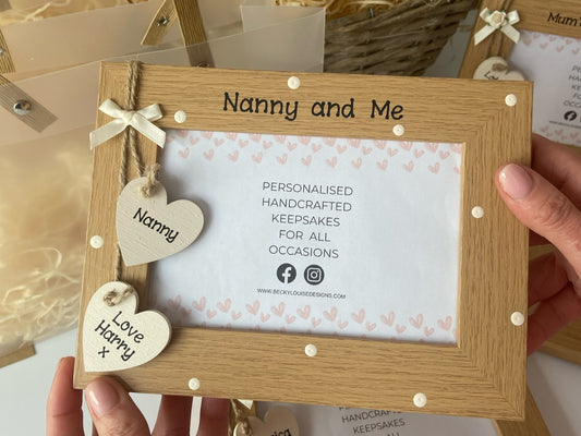Image shows vintage nanny and me photo frame, decorated with cream polka dots and cream wooden hanging hearts with names and a cream bow above