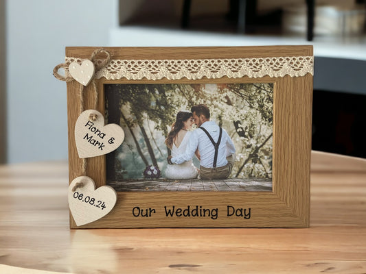 Image shows vintage brown wedding day photo frame, consists of two hanging hearts with names and date, as well as a small dotted heart above, cream lace runs along the top.