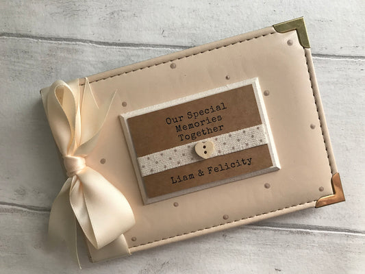 Image shows 6x4 photo album for memories made by couple, decorated with beige polka dots and cream ribbon, also a cream plaque with dotted ribbon and small wooden heart, quote and names printed onto plaque