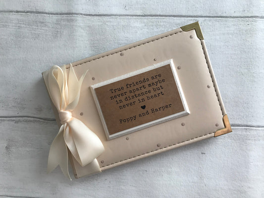 Image shows a friendship photo album, consists of beige polka dots, cream ribbon, cream plaque with friendship quote and names.