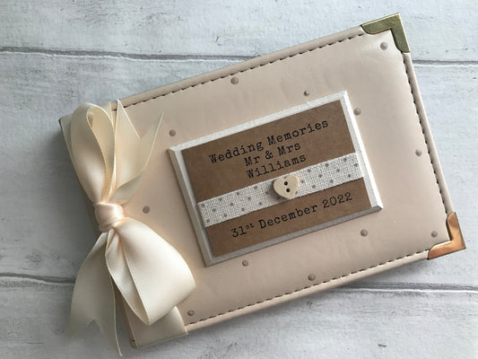 Image shows wedding photo album, decorated with beige polka dots, cream ribbon, cream plaque with dotted ribbon and small wooden heart, text with name and date.