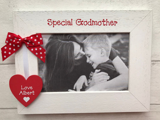 Image shows wooden photo frame for god mother, consists of a small wooden heart with the name of god child, attached to a small piece of white ribbon running up to a dotted bow.
