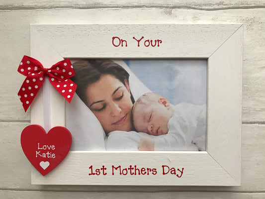 Image shows a first mothers day photo frame, down the side sits a wooden heart with baby's name, attached to white ribbon and a dotted bow.