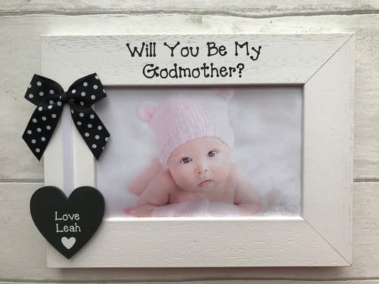 Image shows will you be my godmother photo frame, with a dotted bow on the side attached to a heart with the god child's name with white ribbon.