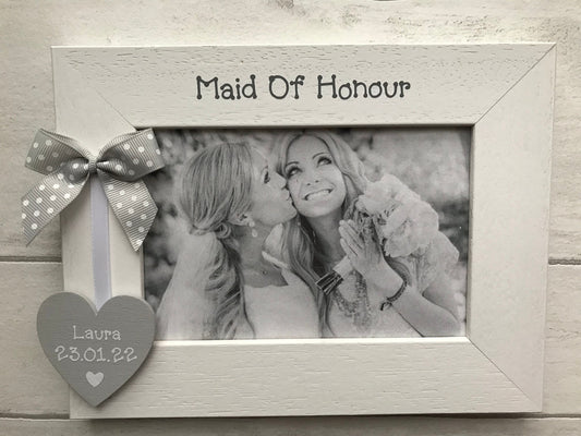 Image shows maid of honour photo frame, consists of wooden heart with maid of honours name and date of wedding, attached to a white piece of ribbon and dotted bow.