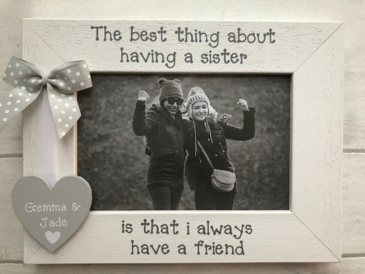 Image shows a sisters photo frame, consists of wooden heart with sisters names attached to a white ribbon and dotted bow.