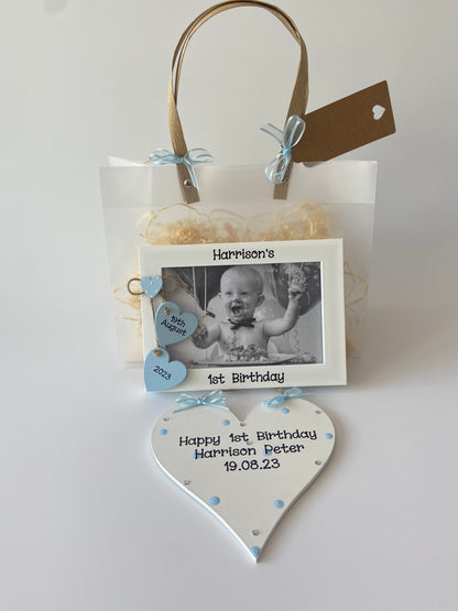 Image shows matching photo frame and plaque for 1st birthday, photo frame consisting of two hanging hearts with date of birthday and a small heart decorated with white polka dots, plaque decorated with polka dots, gems and ribbon. Includes gift wrap and photo of your choice